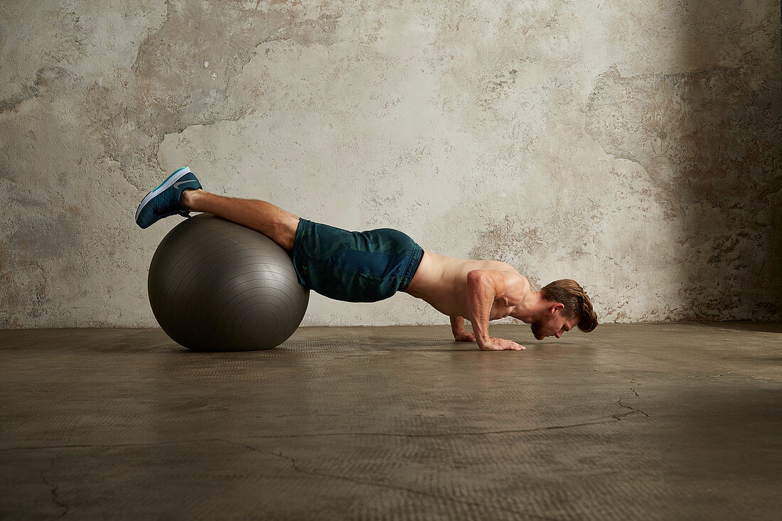 A young man doing push-ups with his legs on a physio ball