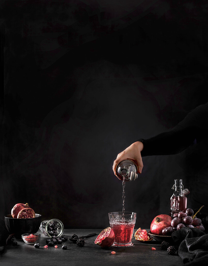 Hand pouring pomegranate juice from bottle to glass on black background