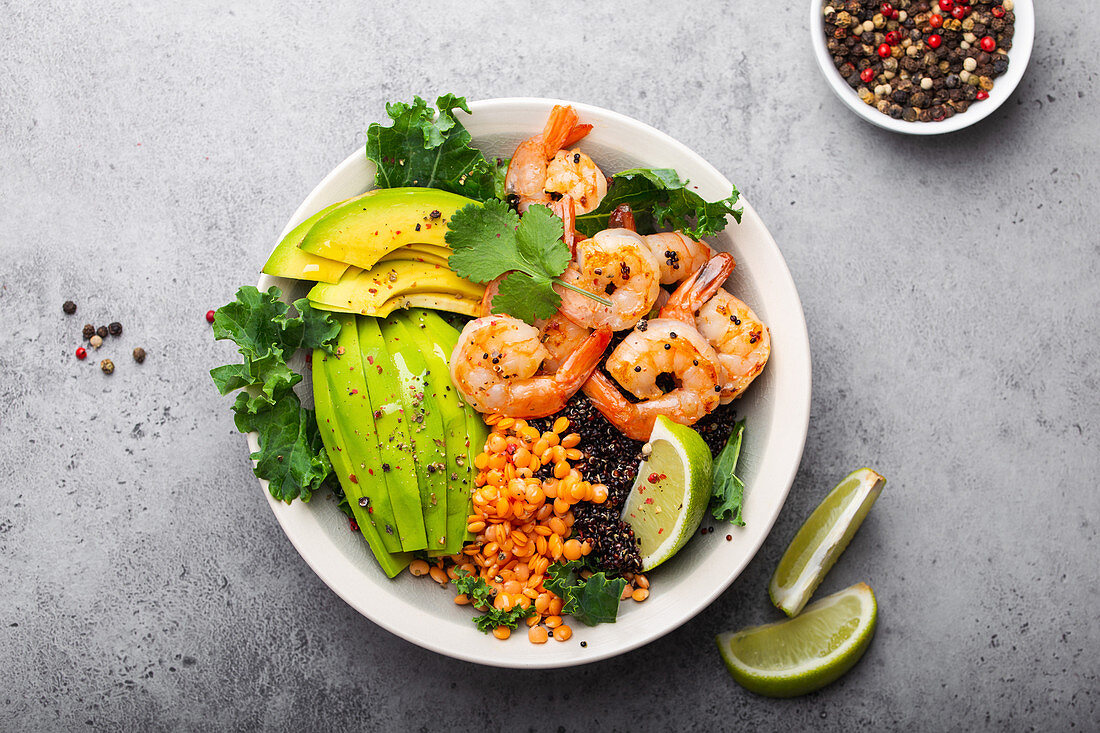 Salatschüssel mit Garnelen, Avocado, Kohl, Quinoa, roten Linsen, Limetten und Olivenöl