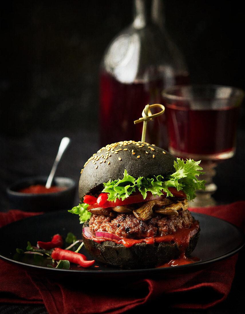 A black burger with mushrooms, peppers and salad