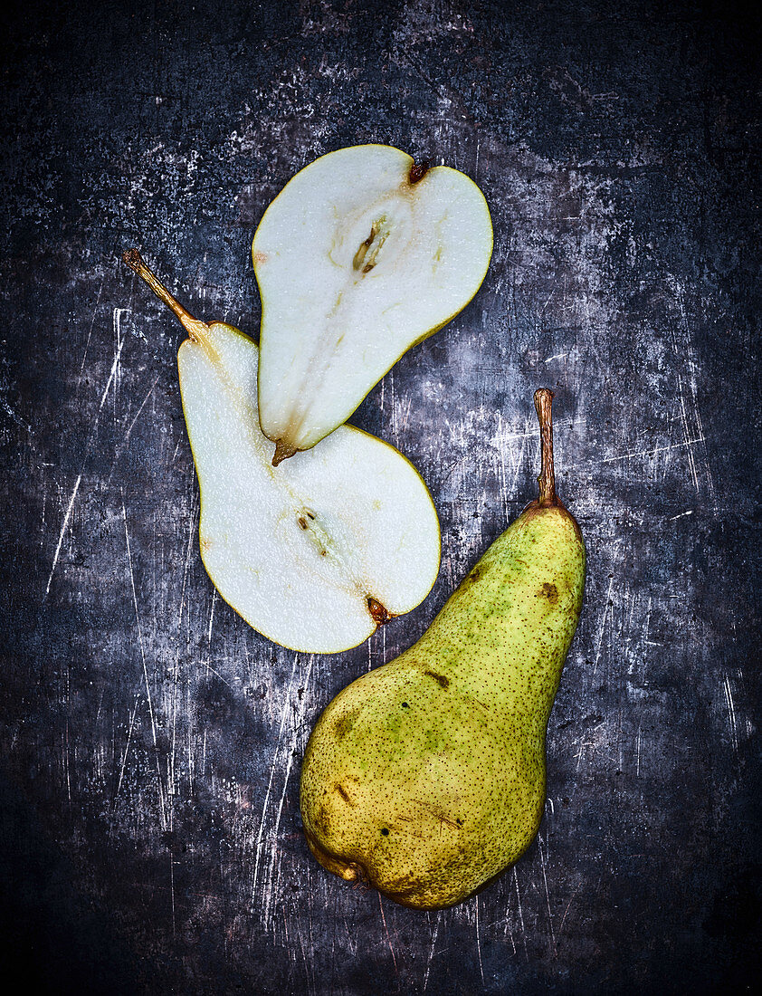 A whole pear and a halved pear on a grey metal surface