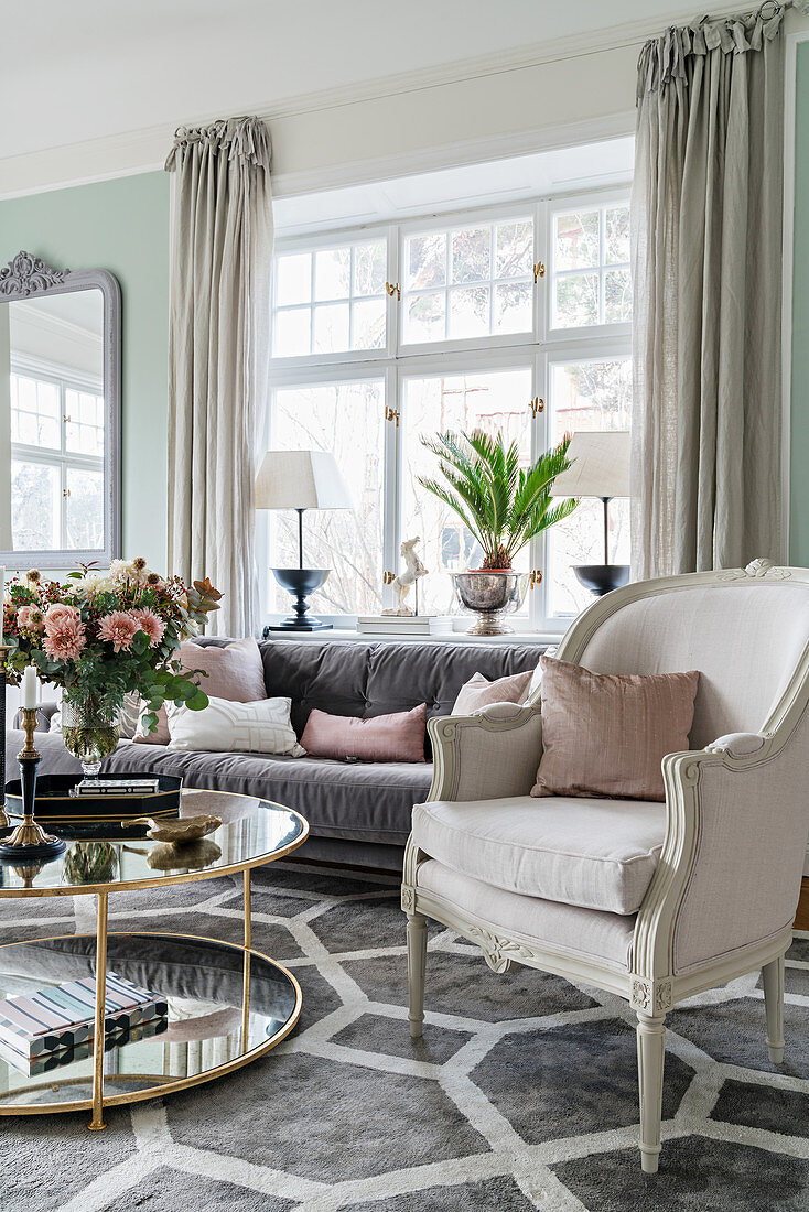 Stylish seating around round table in light-flooded living room with pastel-green walls