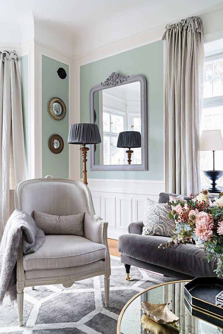 Armchair and sofa in light-flooded living room with pastel-green walls