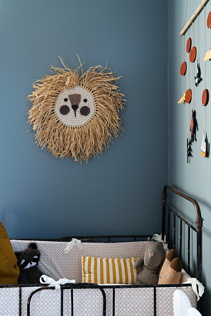 Löwenkopf aus Bast an blauer Wand überm Bett im Kinderzimmer