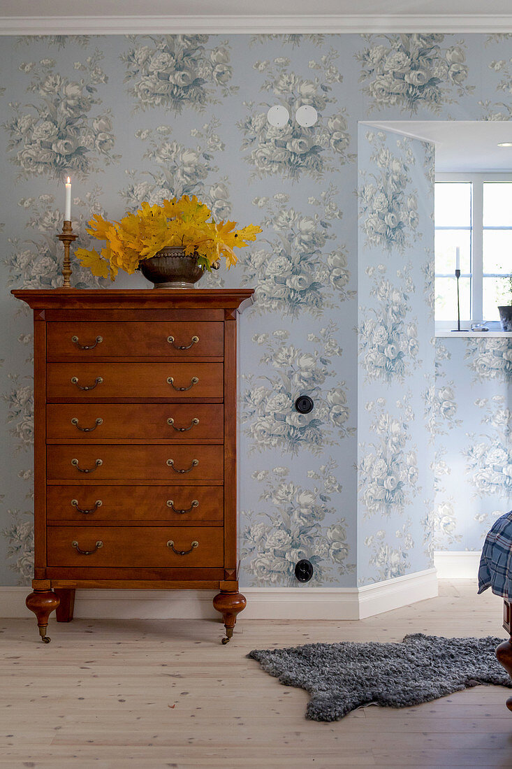 Antike Hochkommode in Schlafzimmer mit nostalgischer hellblauer Blumentapete