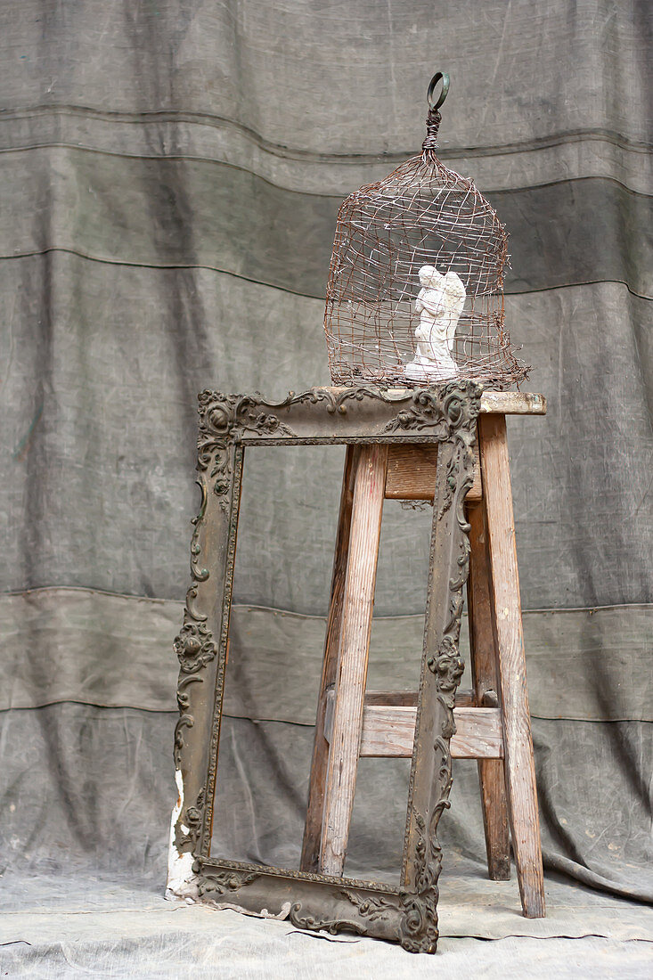 Angel figurine in cage on wooden stool and antique picture frame