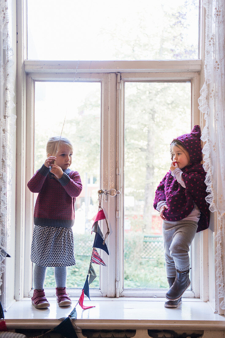 Two girls wearing sustainable fashion stood in period window