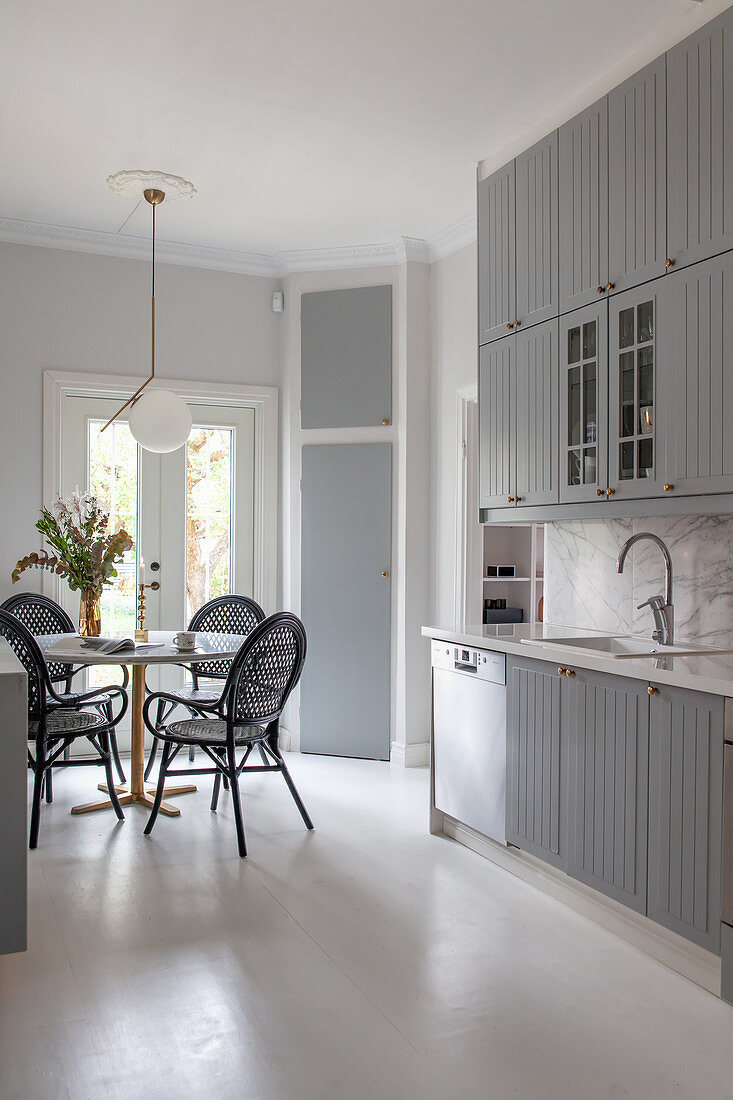 Black rattan chairs around round table in grey kitchen-dining room