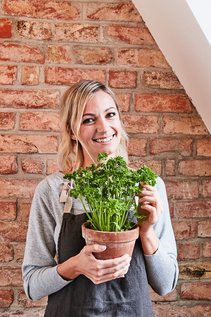 A woman with an apron holds a clay pot with fresh parsley