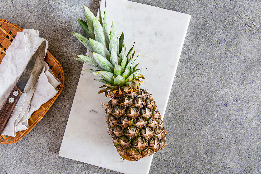 Fresh pineapple on a white marble platter on a stone surface