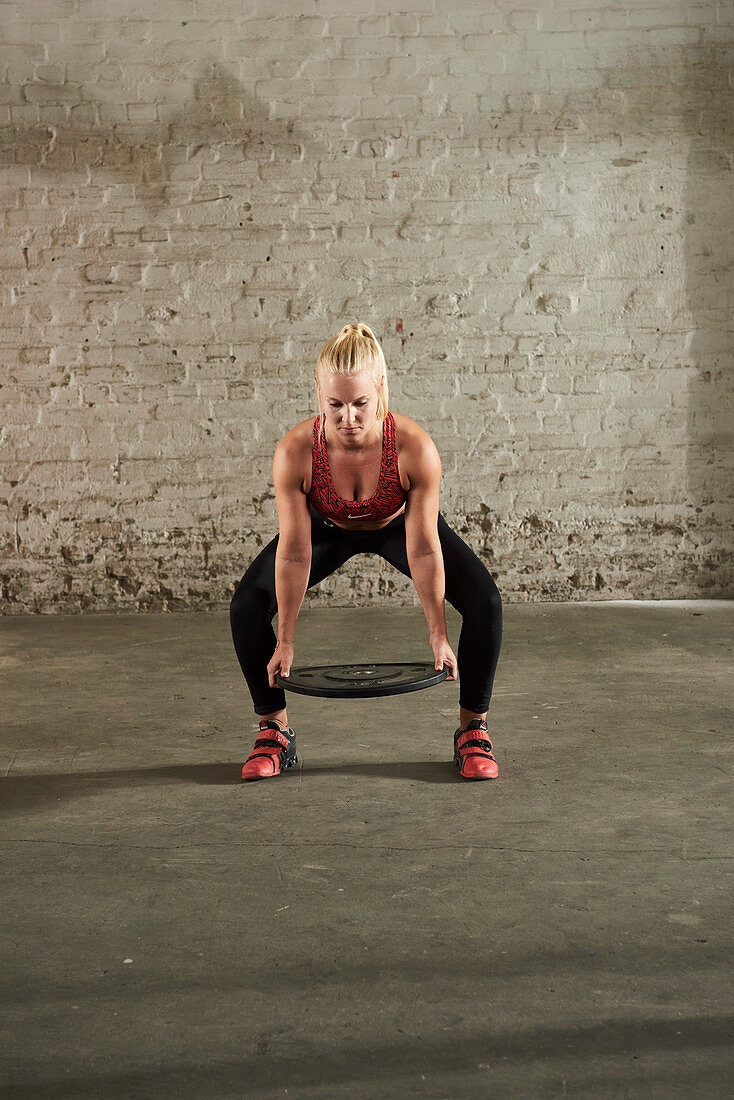 A young woman holding a weight plate at calf height