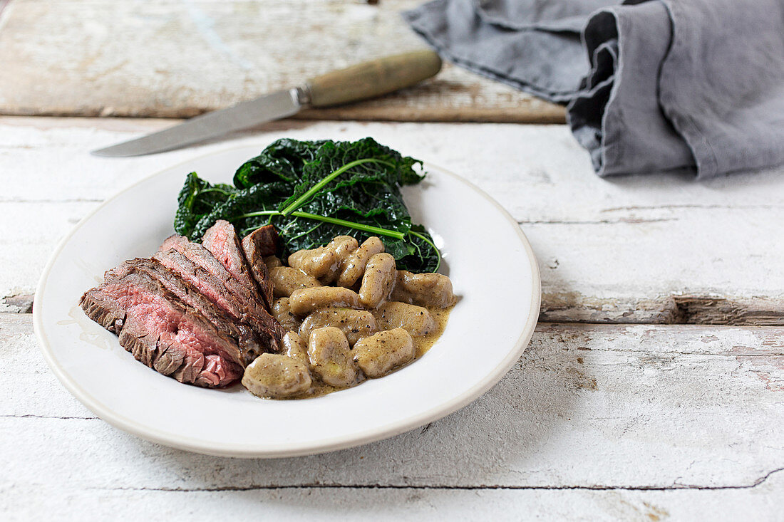 Steak, Gnocci and Cavelo Nero served on a white plate on a rustic white board