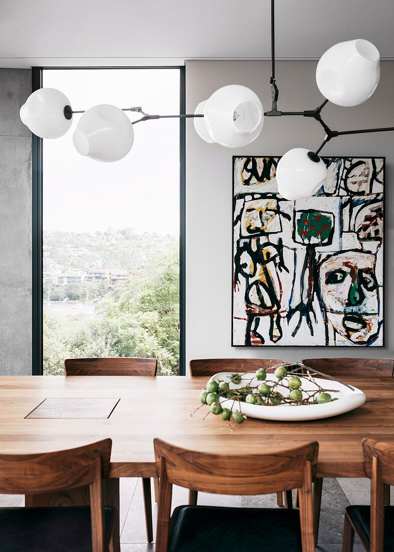 Designer lamp above the wooden dining table in front of the vertical window