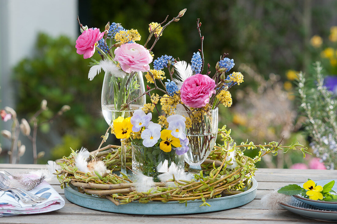 Table decoration with ranunculus, horn violet, grape hyacinth and cornelian cherry in a wicker wreath