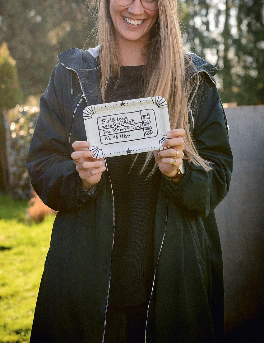 Smiling woman holding invitation to BBQ written on paper plate