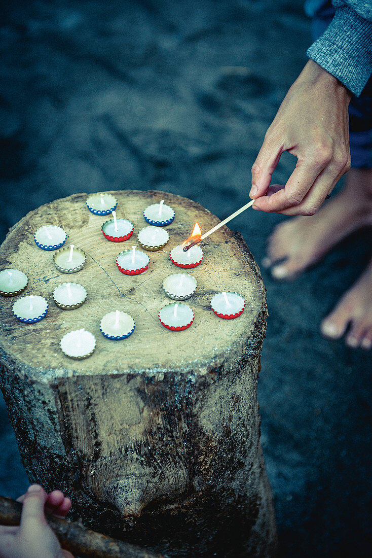 Hand lighting tiny candles in bottle caps