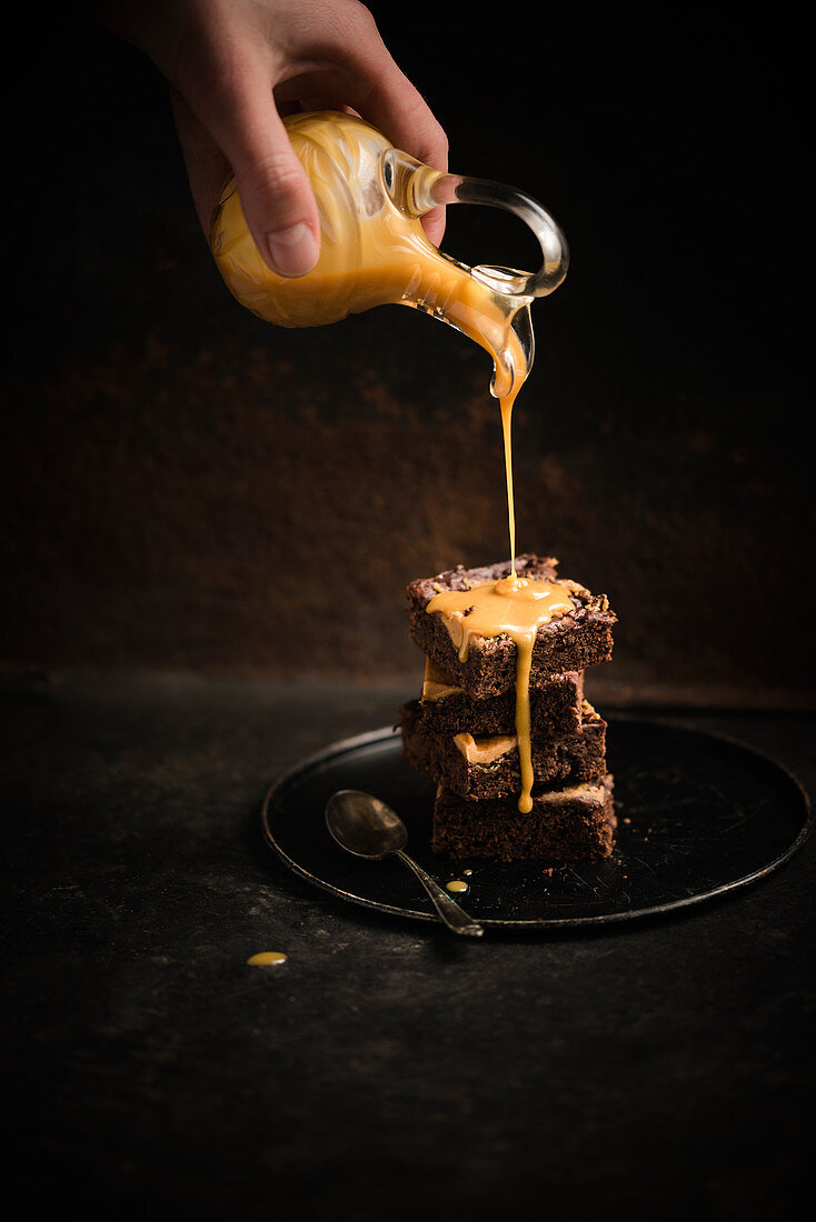 A woman pouring salted caramel over vegan sweet potato and peanut brownies