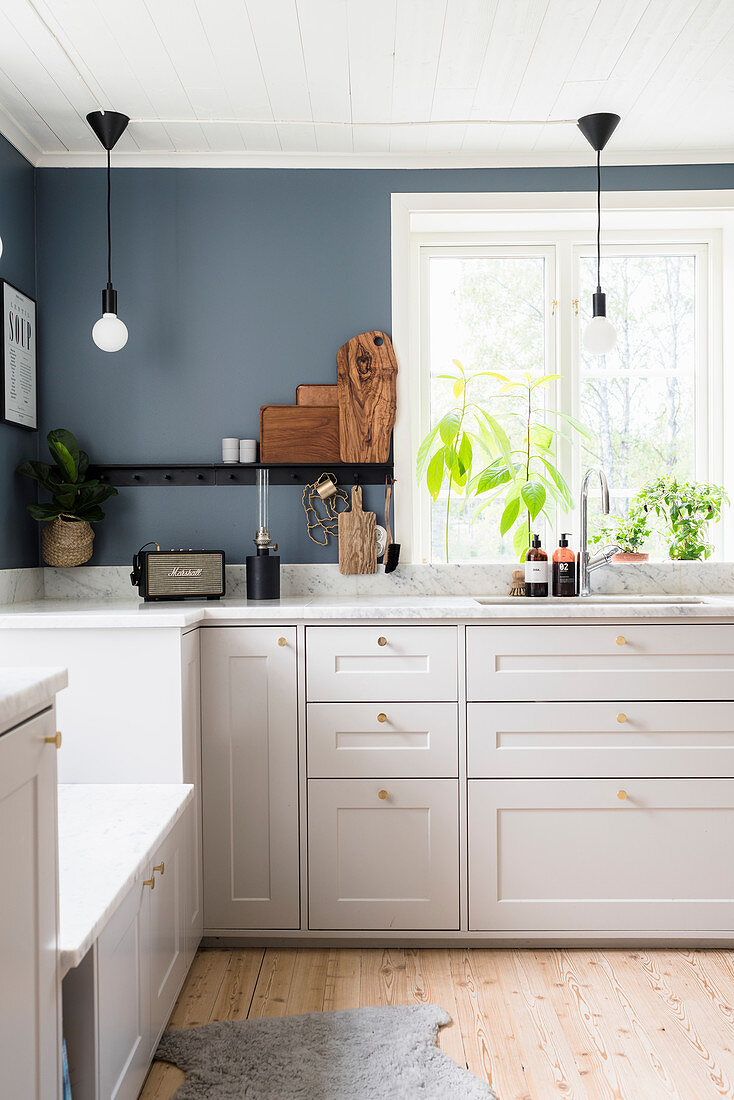 White kitchen counter with marble worksurface below window in kitchen with grey-blue walls