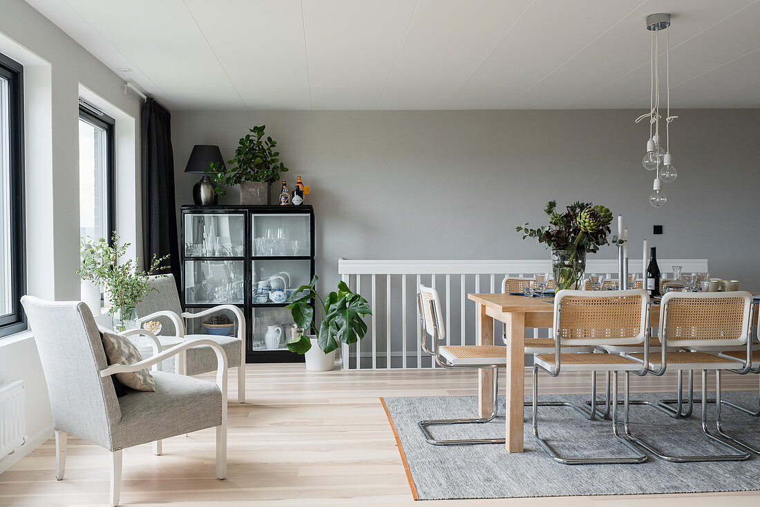 Black cabinet, pale wooden dining table and cane chairs in interior with pale grey walls