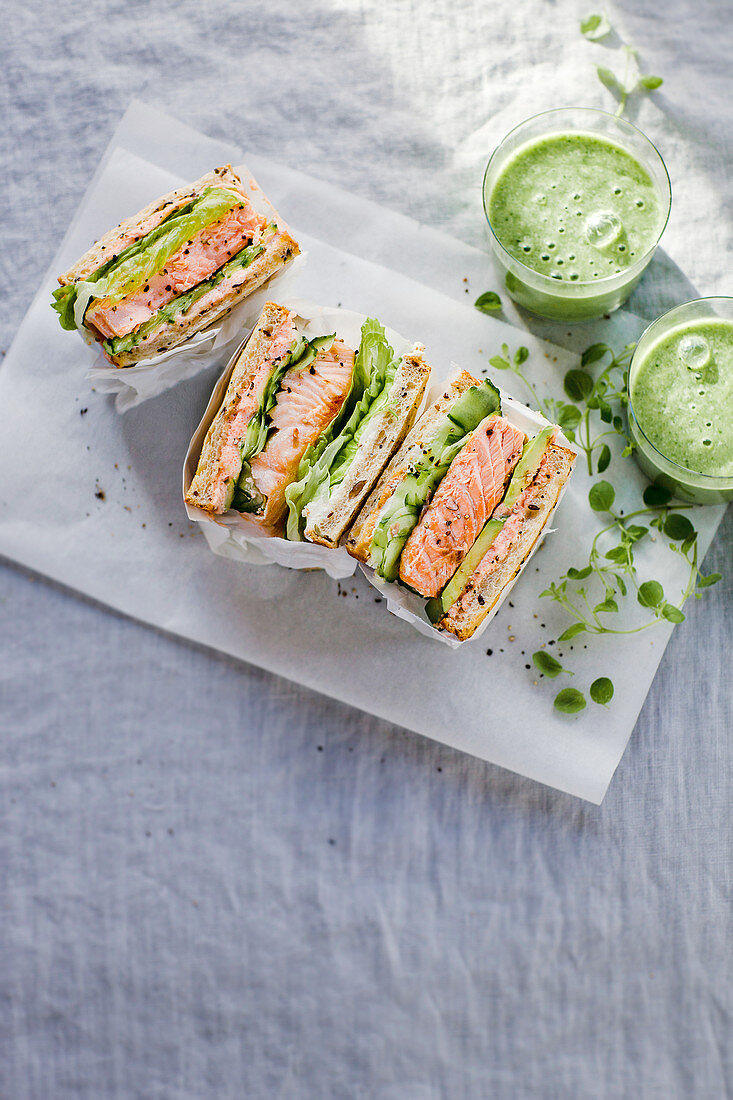 Toast-Sandwiches mit Lachs, Gurke, Avocado und Kaviarcreme, serviert mit grünem Smoothie