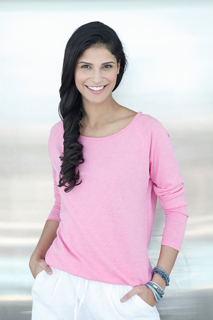 A dark-haired woman wearing a pink jumper and white shorts