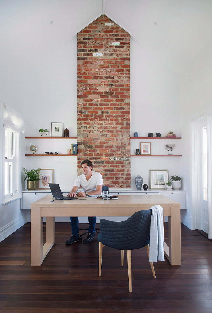 Man at large desk in front of fireplace with exposed brickwork