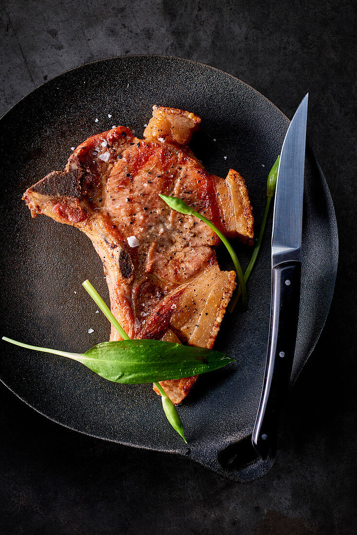A fried pork chop on a plate with a knife