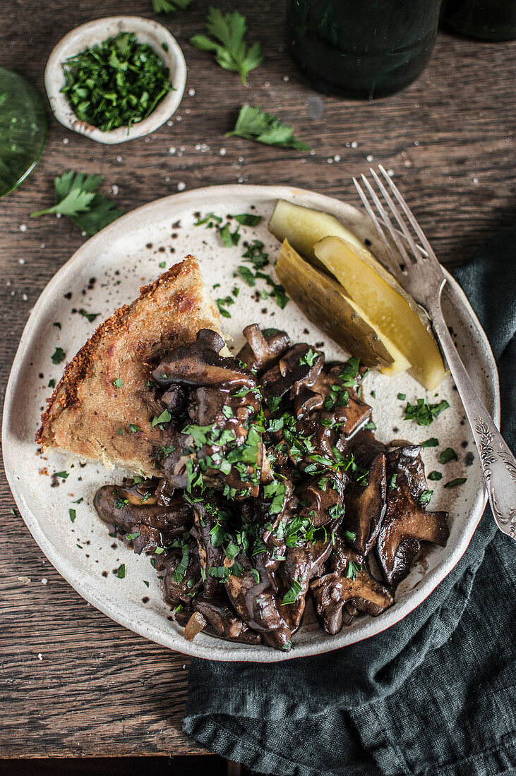 Ein Stück Kartoffelkuchen mit Champignons, Petersilie und fermentierten Gurken