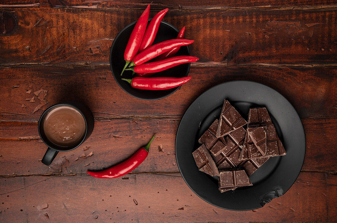 Mug of fresh hot drink placed on lumber tabletop near plate with pieces of chocolate and chili pepper