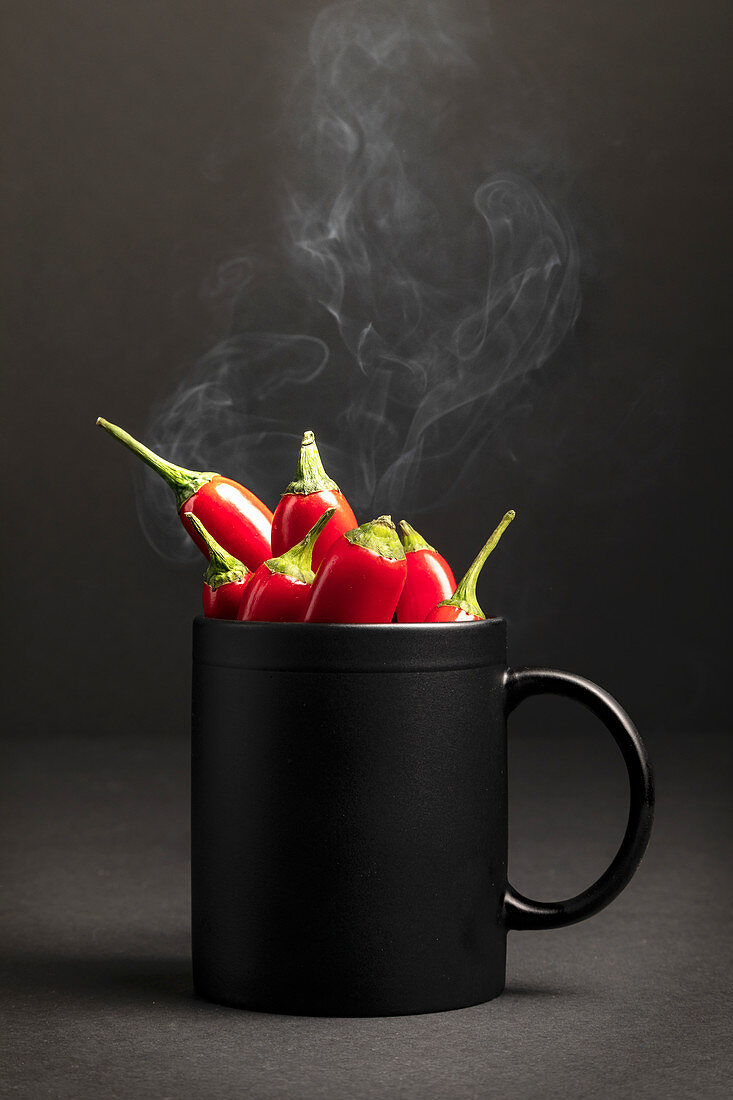 Steamy black ceramic mug full of hot chili peppers placed against dark background