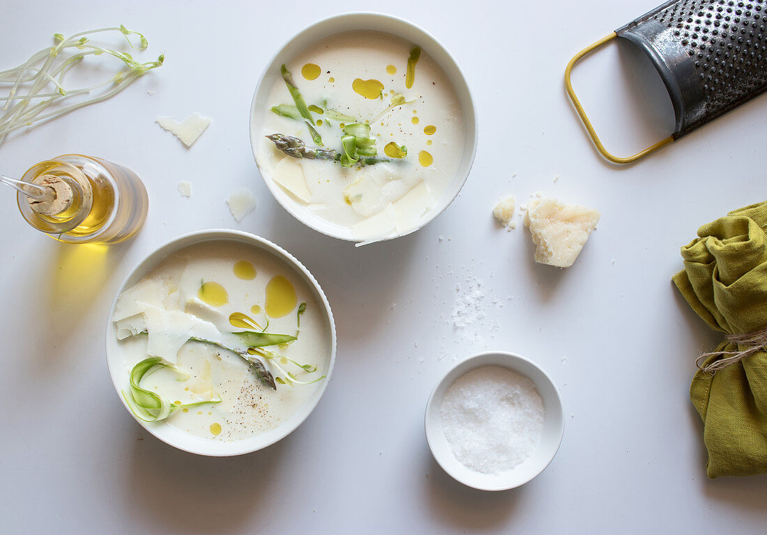 Grater and napkin placed near oil with salt and two bowls of yummy asparagus cream soup with cheese and herbs