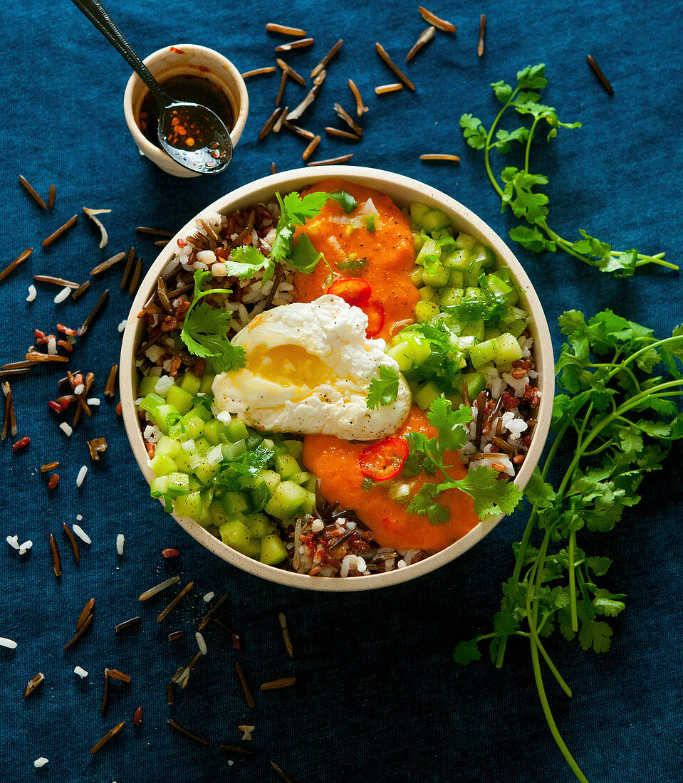 A bowl with rice, cucumber, tomato sauce and a poached egg