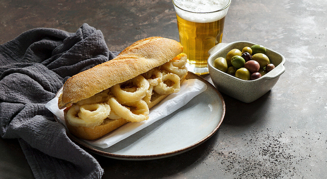 Bocadillo con calamares (Tintenfisch-Sandwich, Spanien) mit Oliven und Bier