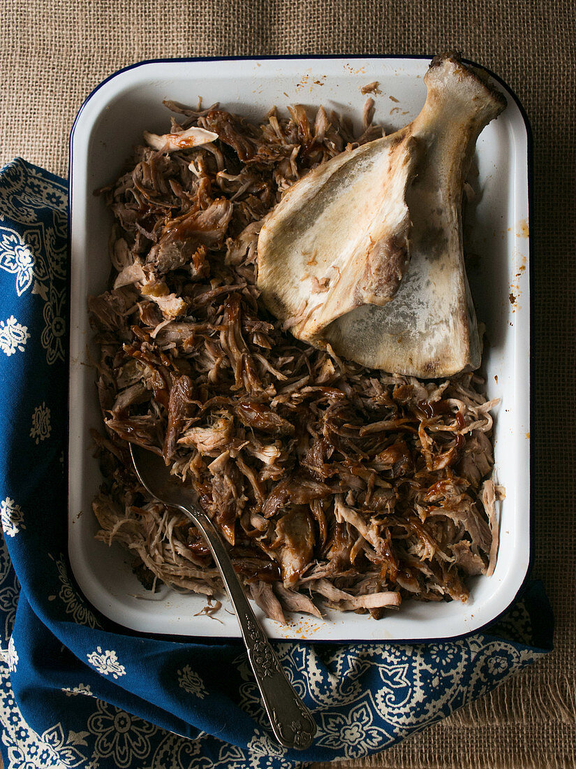 Metal bowl with delicious pulled pork and clean bone placed on ornamental and linen napkins