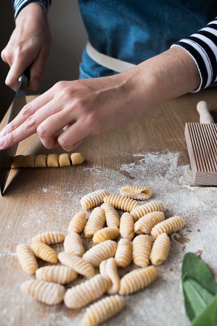 Anonymous female cutting dough for homemade gnocchetti pasta on table in kitchen