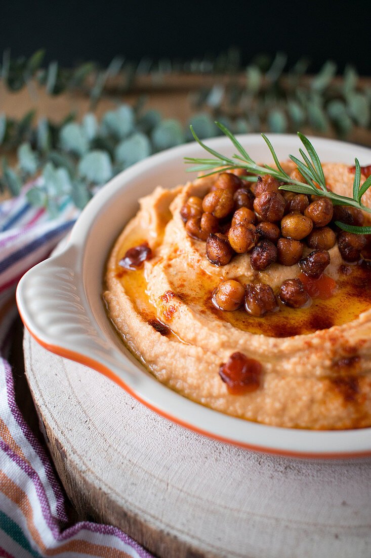 Fresh sprig of rosemary placed on top of delicious pepper hummus with chickpea in kitchen