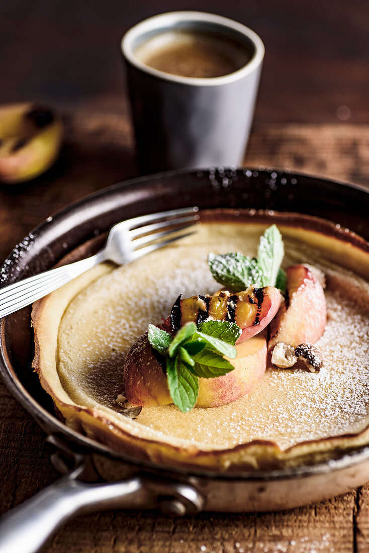 Dutch baby pancake with grilled peaches, mint, pwdered sugar and hazelnuts