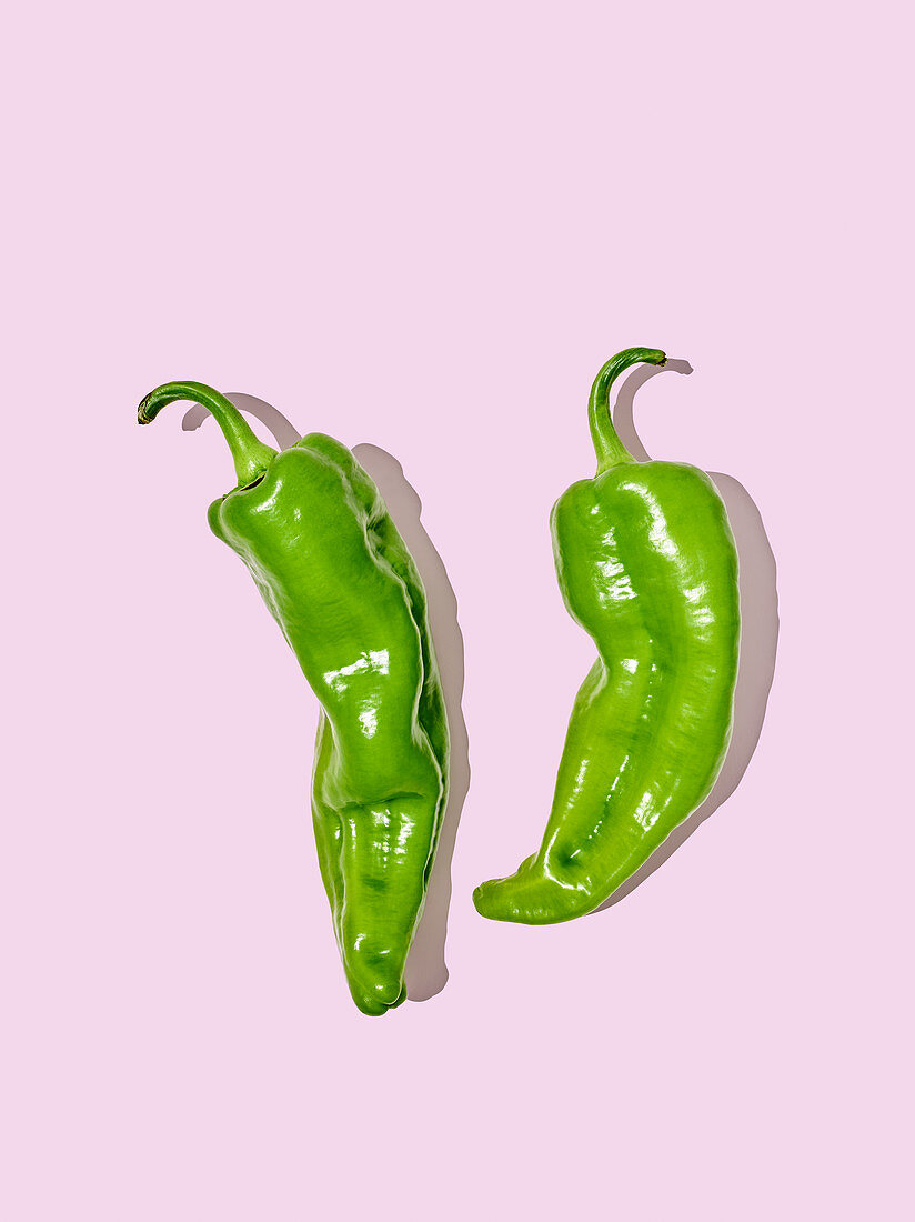 Two green chilli peppers on a pink surface