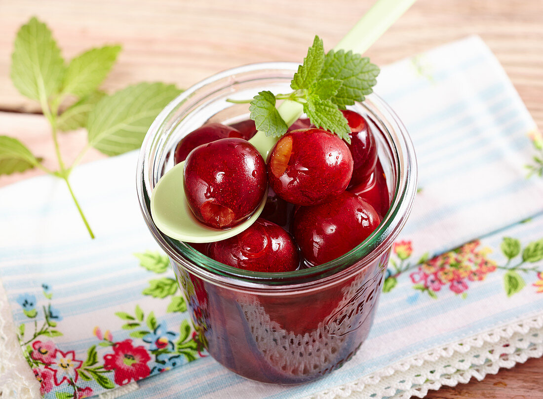 Sweet-and-sour cherry compote in a jar with lemon balm