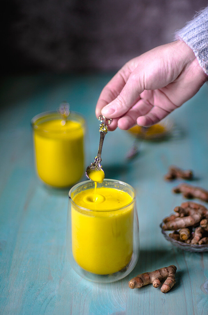 Milk with turmeric (golden milk) and fresh turmeric root on a blue background