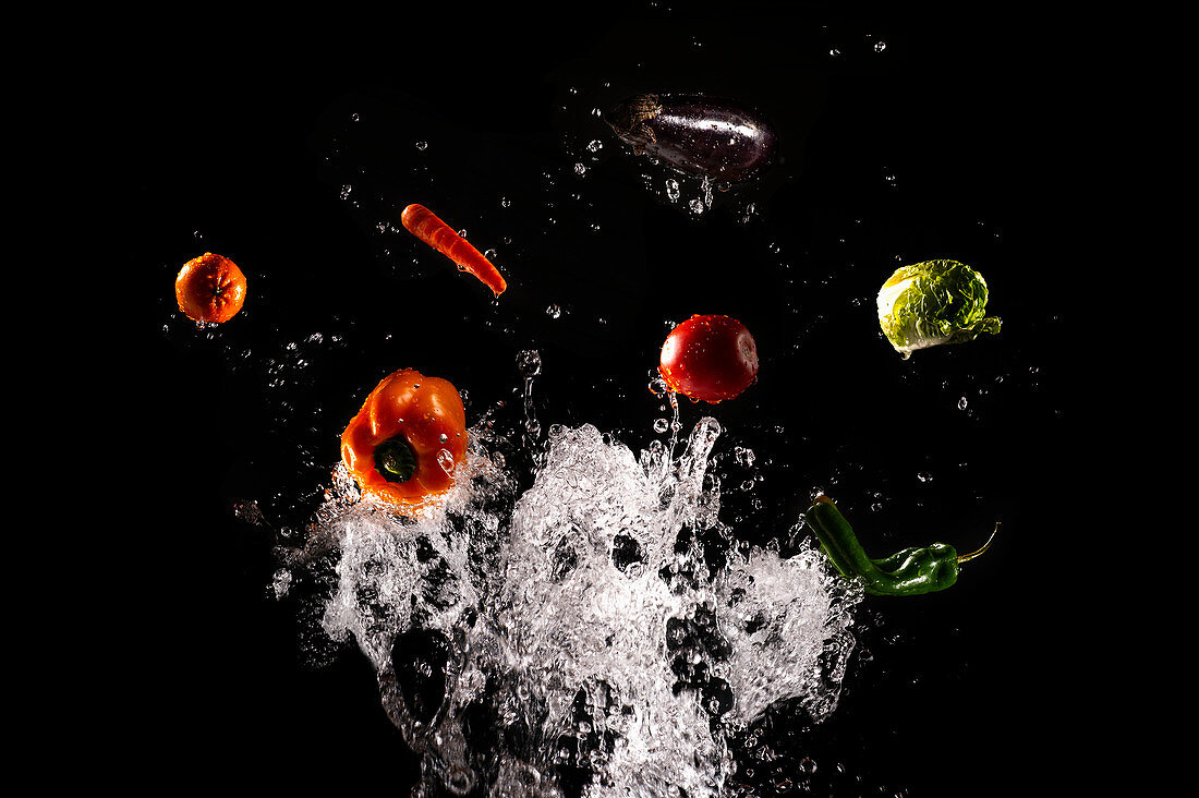 Levitating ripe vegetables and salad in clear splashes of water on black background