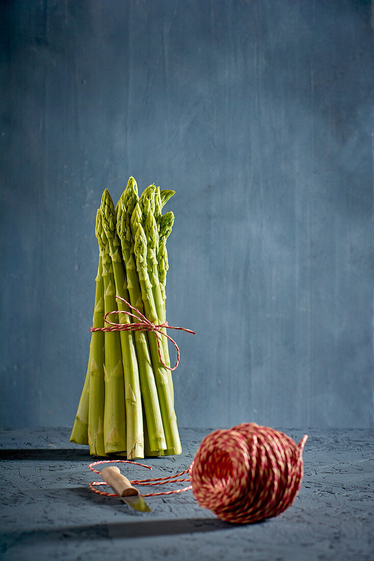 A bundle of green asparagus with a ball of kitchen twine in the foreground