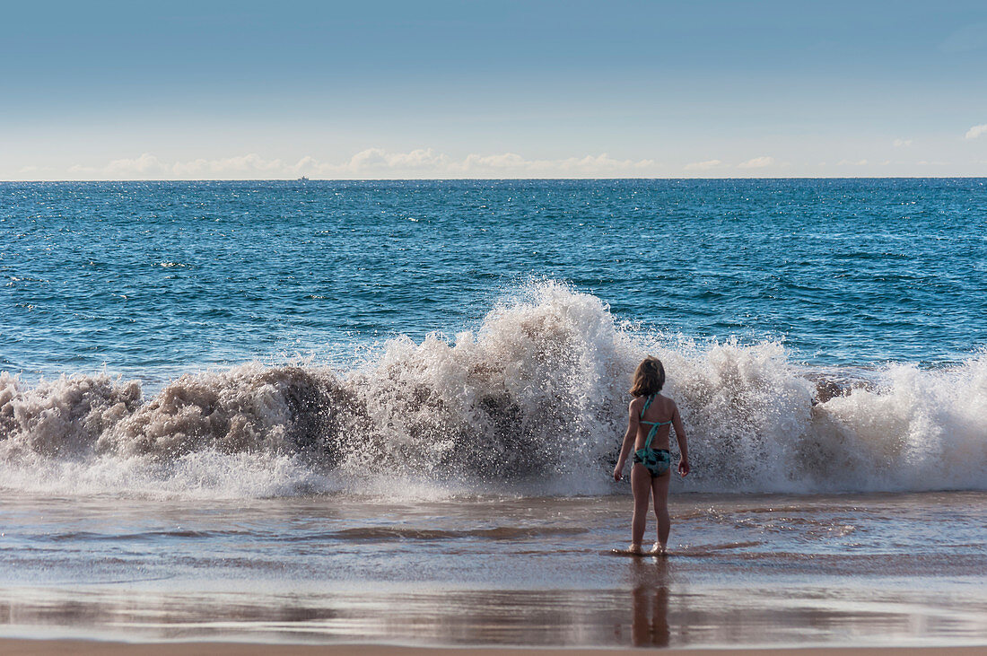 A young girl faces a big wave on the beach, Hawaii