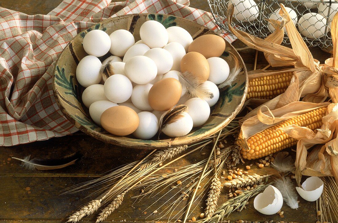 weiße & braune Eier in einer Schale, neben Getreide & Mais