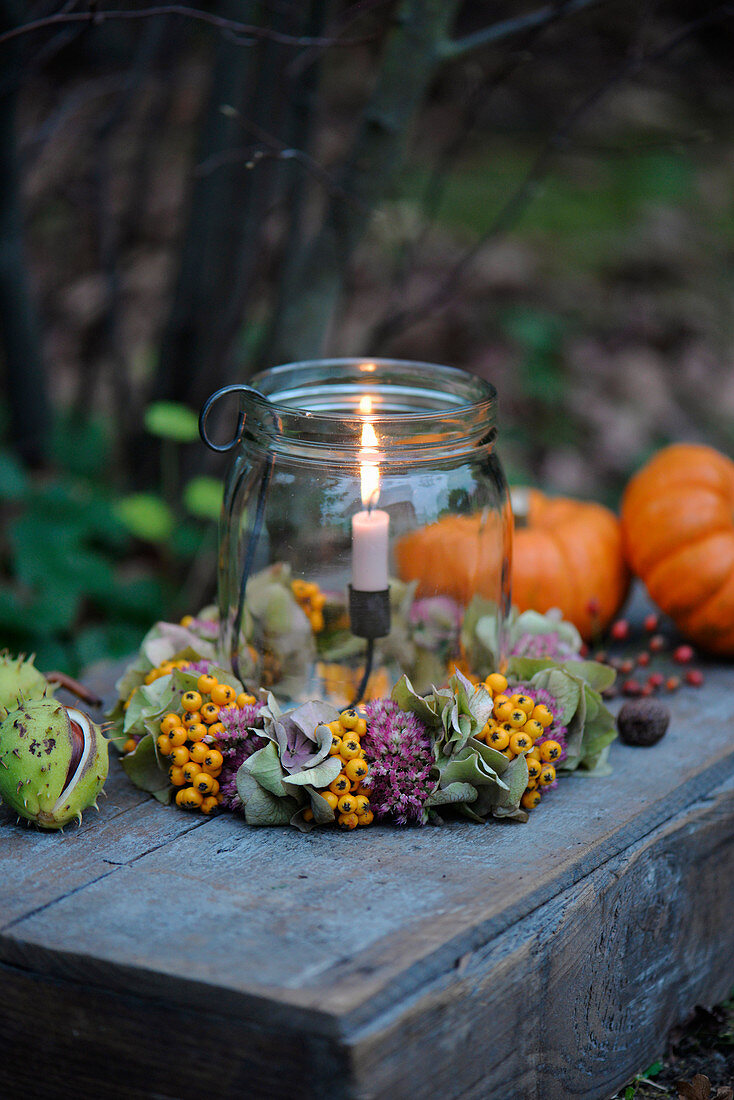 Windlicht mit Kränzchen aus Fetthenne, Hortensienblüten und Vogelbeeren, daneben Zierkürbisse und Kastanien