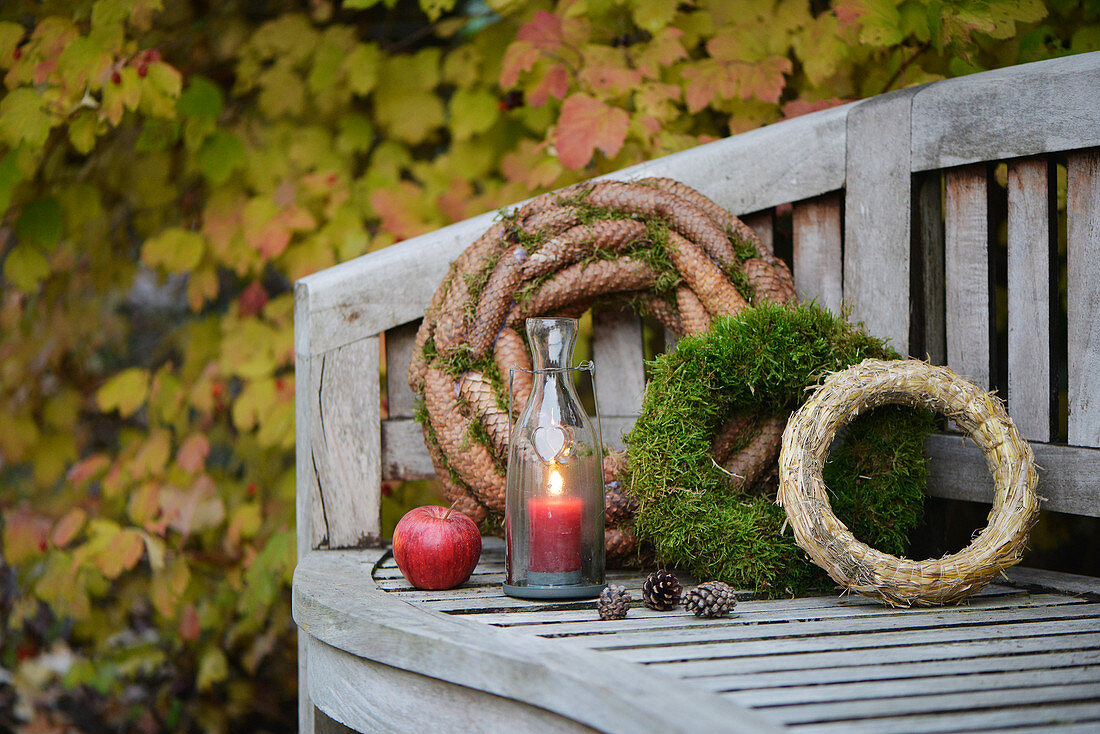 Gartenbank dekoriert mit Kränzen (Moos, Fichtenzapfen und Strohkranz) und Windlicht