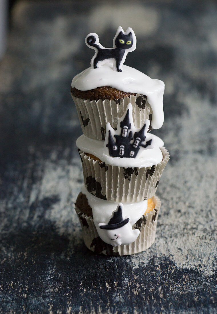 Chocolate muffins decorated with icing and a sugar haunted house, a black cat and a ghost