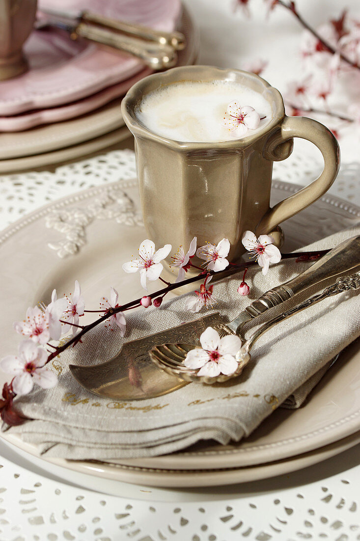 Tasse Cappuccino auf Gedeck in Beige mit Blütenzweig