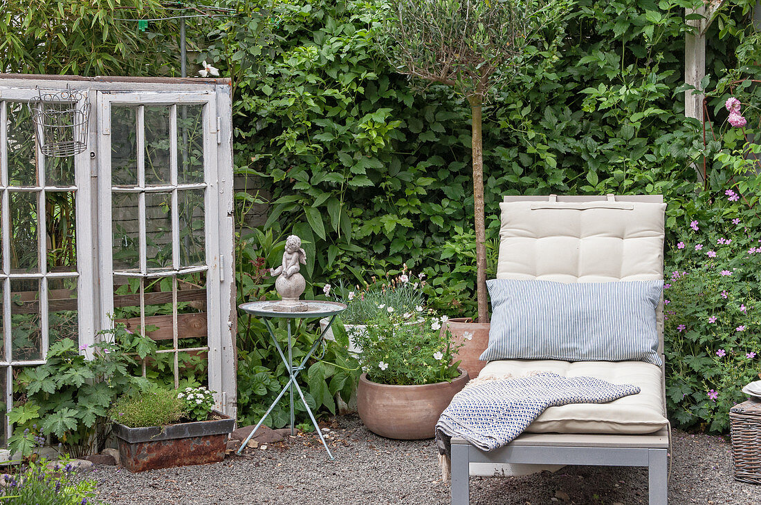 Ruheecke im Garten mit Sonnenliege, antikem Fenster und Dekoration