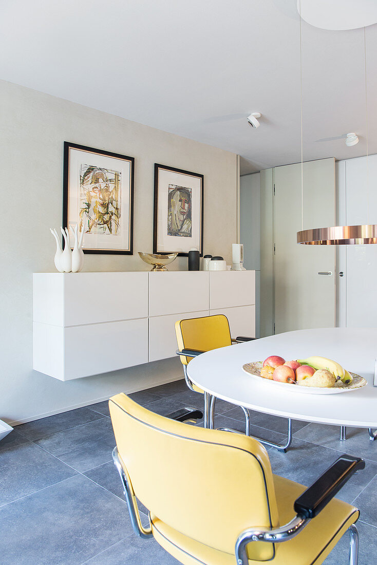 Open-plan dining area with round table, cantilever chairs, floating sideboard and artworks on wall